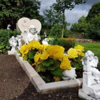 Grabgestaltung mit gelber Bepflanzung und Grabfiguren